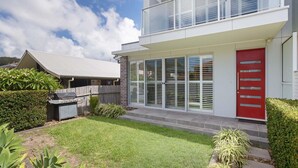 A modern two-story house with a red door, large sliding glass windows, and a well-maintained lawn. - 7 Judith Street - Stunning duplex with ducted air (Corlette)