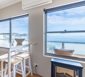 A room with a table and chairs, a window with a view of a body of water, and an air conditioning unit. - Blue Vista,9,13 Victoria Parade - Studio with stunning water views and air conditioning (Nelson Bay)