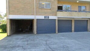 A two-story building with a brick facade, three garage doors, and a 'No Parking on Concrete or Grass' sign.