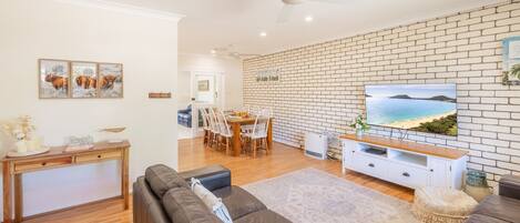 A living room with a brick wall, a television, and a dining area with chairs and a table.
