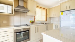 Una cocina moderna con armarios color beige, una campana extractora de acero inoxidable, horno empotrado, un lavamanos y un refrigerador.