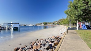 Une plage avec des bateaux amarrés, une aire de jeux et un ciel dégagé.
