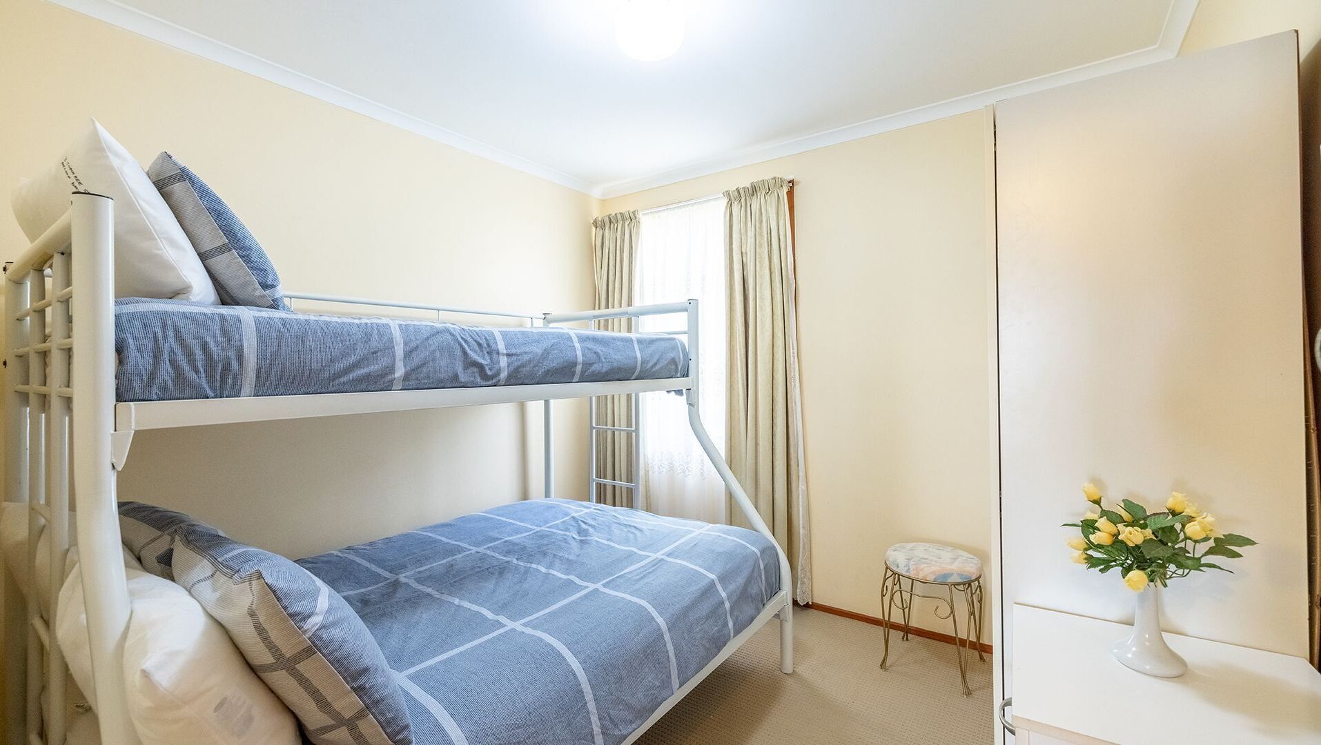 A bunk bed room with a small stool and a vase of flowers.