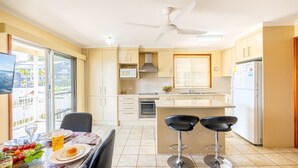 Una cocina moderna con comedor, que cuenta con un gran ventanal, un ventilador de techo y un horno empotrado.
