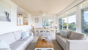 Un salon spacieux doté d’une grande fenêtre, d’un ventilateur de plafond et d’un coin repas avec une table et des chaises.