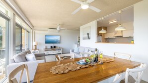 Un salon moderne avec une table à manger en bois, mise pour le repas, un canapé, un téléviseur et un ventilateur de plafond.