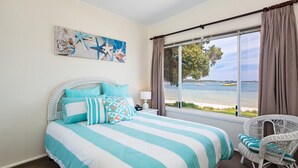 A bedroom with a large window, a bed with striped bedding, a chair, and a painting on the wall. - Casa Martins, 219 Foreshore Drive - Absolute Waterfront House (Salamander Bay)