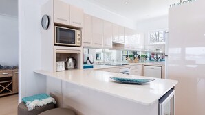 A modern kitchen with a central island, a microwave, and a clock on the wall. - Casa Martins, 219 Foreshore Drive - Absolute Waterfront House (Salamander Bay)