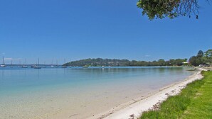 A beach with clear water, a sandy shore, and boats in the distance. - Casa Martins, 219 Foreshore Drive - Absolute Waterfront House (Salamander Bay)
