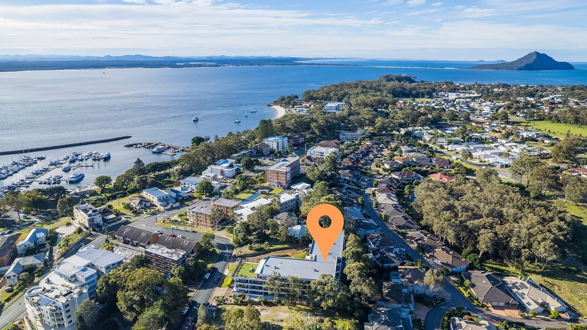 An aerial view of a coastal town with residential buildings, a marina, and a prominent mountain in the distance.