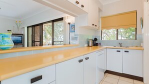A modern kitchen with white cabinets, a wooden countertop, and a window with a view of trees.