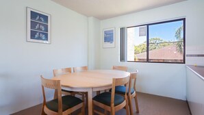 Une pièce avec une table ronde en bois et six chaises, une fenêtre donnant sur des immeubles et deux tableaux encadrés accrochés au mur.
