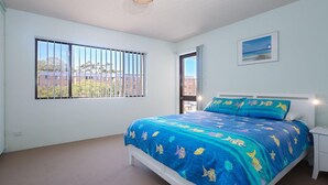 Une chambre à coucher avec un lit, une table de chevet, une fenêtre avec des barreaux et un tableau accroché au mur.