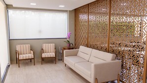 Una habitación con un sofá color beige, dos sillones estampados, una pequeña mesita con una orquídea en maceta y un panel de madera decorativo.