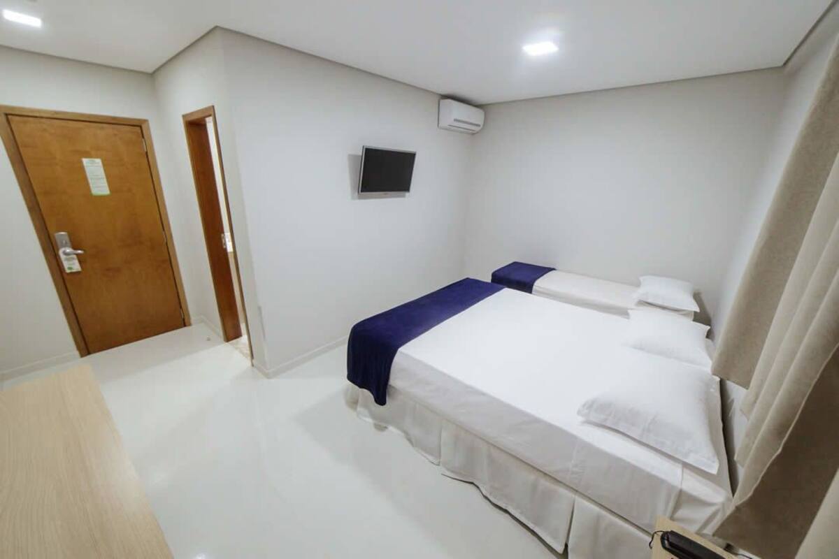 A bedroom with two beds, a wooden door, a flat-screen TV, and a white air conditioning unit on the wall.