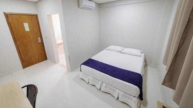 Un dormitorio con una cama, una silla, una puerta de madera, un equipo de aire acondicionado y una cortina.