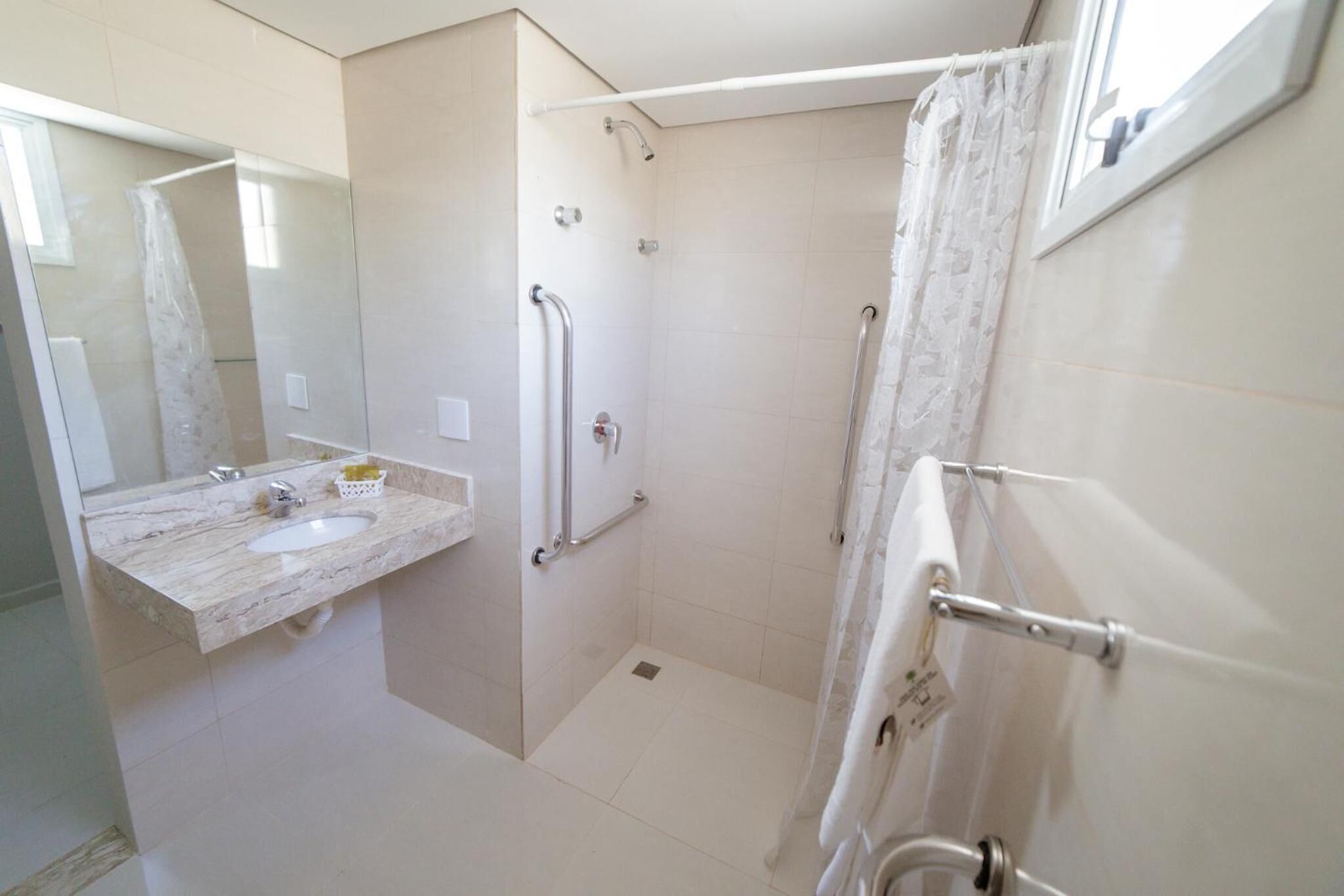 Un bagno con lavabo in marmo, cabina doccia in vetro e tenda da doccia bianca.
