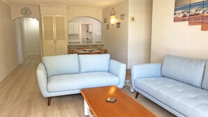 Una sala de estar con un sofá azul claro, una mesa de centro de madera y una cocina al fondo.