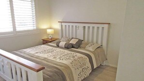 Un dormitorio con cama, mesita de noche, lámpara y ventana con persianas.
