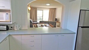 Una cocina compacta con microondas, hervidor y refrigerador. Se observa, a través de un arco, un área de comedor con una mesa y sillas.