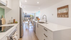 A modern kitchen with a central island, stainless steel appliances, and a wooden number clock on the wall. - The Shoal, 104/6-8 Bullecourt Street - linen included & under 200m to beach (Shoal Bay)