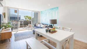 Uma sala de estar moderna com área de jantar, um conjunto de sofá, uma mesa de centro com petiscos e uma grande janela com vista.