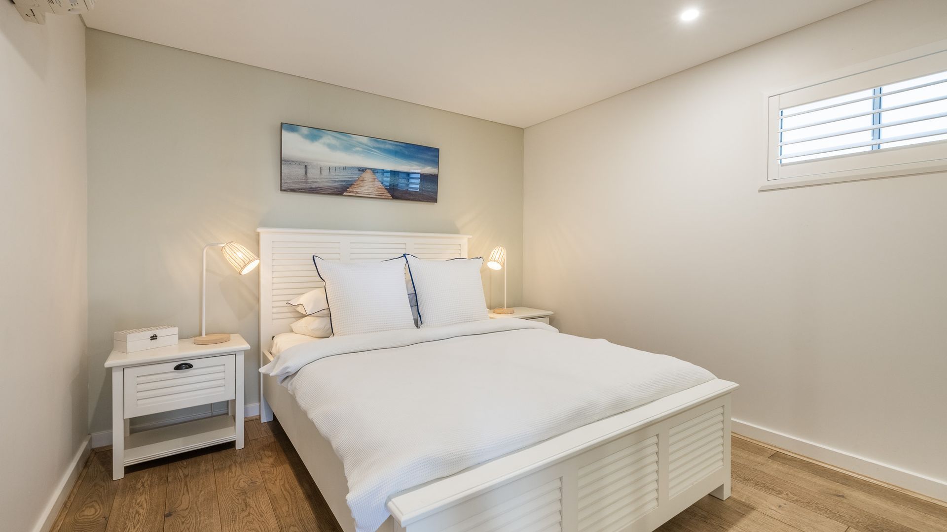 Une chambre à coucher avec un lit, des tables de chevet, une commode, un tableau au mur et une fenêtre.