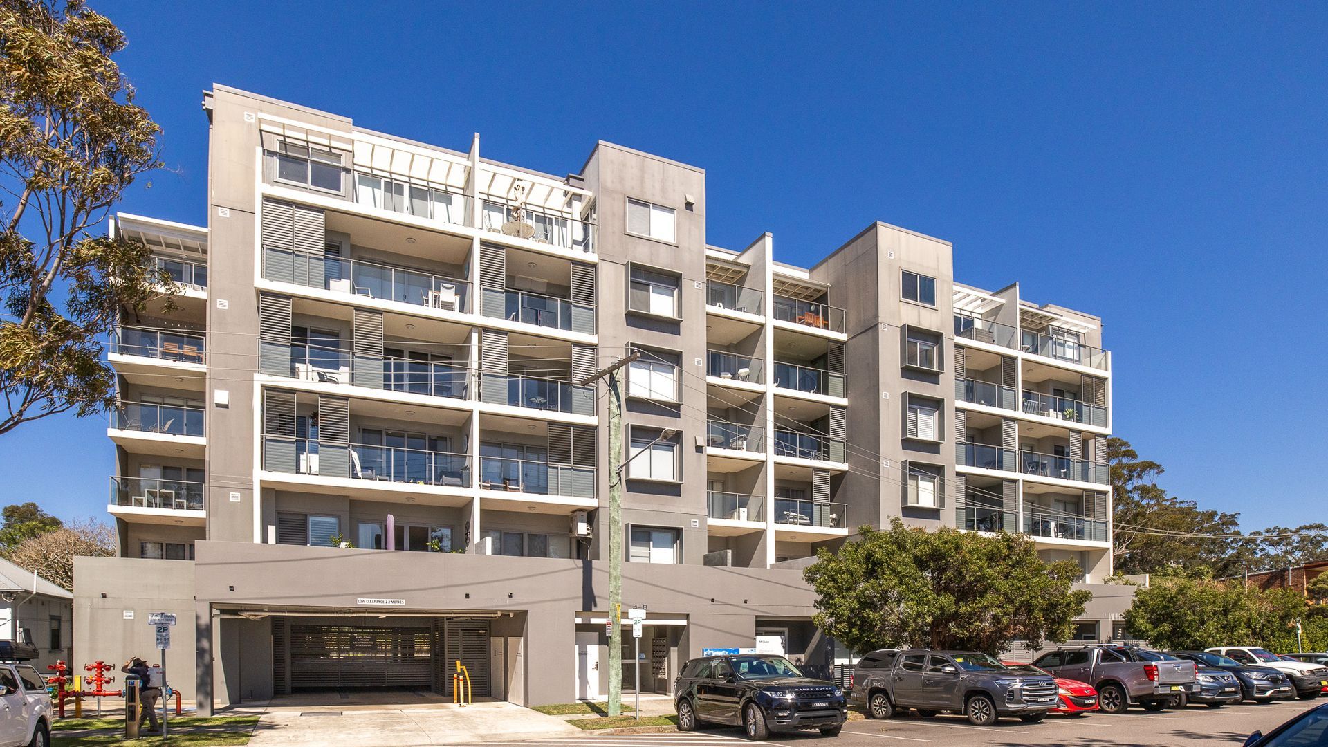 Un immeuble résidentiel à plusieurs étages, doté de balcons, d’une entrée de garage et d’un espace de stationnement où sont garées des voitures.
