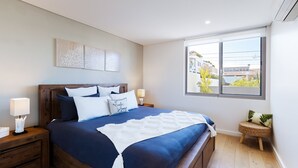 Une chambre à coucher avec un grand lit, deux tables de chevet, une fenêtre avec vue et une œuvre d’art accrochée au mur.