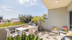 A balcony with a table and chairs, a potted plant, and a view of the surrounding area. - The Shoal, 104/6-8 Bullecourt Street - linen included & under 200m to beach (Shoal Bay)