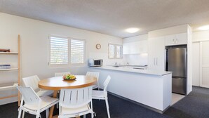 Eine moderne Küche mit weißen Schränken, einem Edelstahl-Kühlschrank und einem Essbereich mit Holztisch und weißen Stühlen.