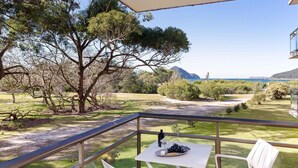 Ein Balkon mit Tisch, gedeckt für eine Mahlzeit, mit Blick auf eine grüne Landschaft mit Bäumen und Meer.