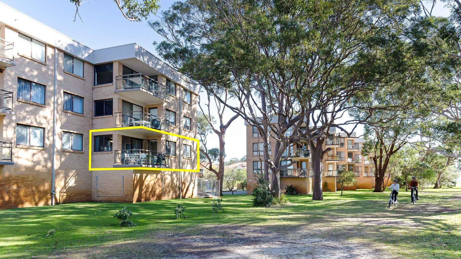 Un edificio residencial de varios pisos con balcones, rodeado de árboles y un césped.