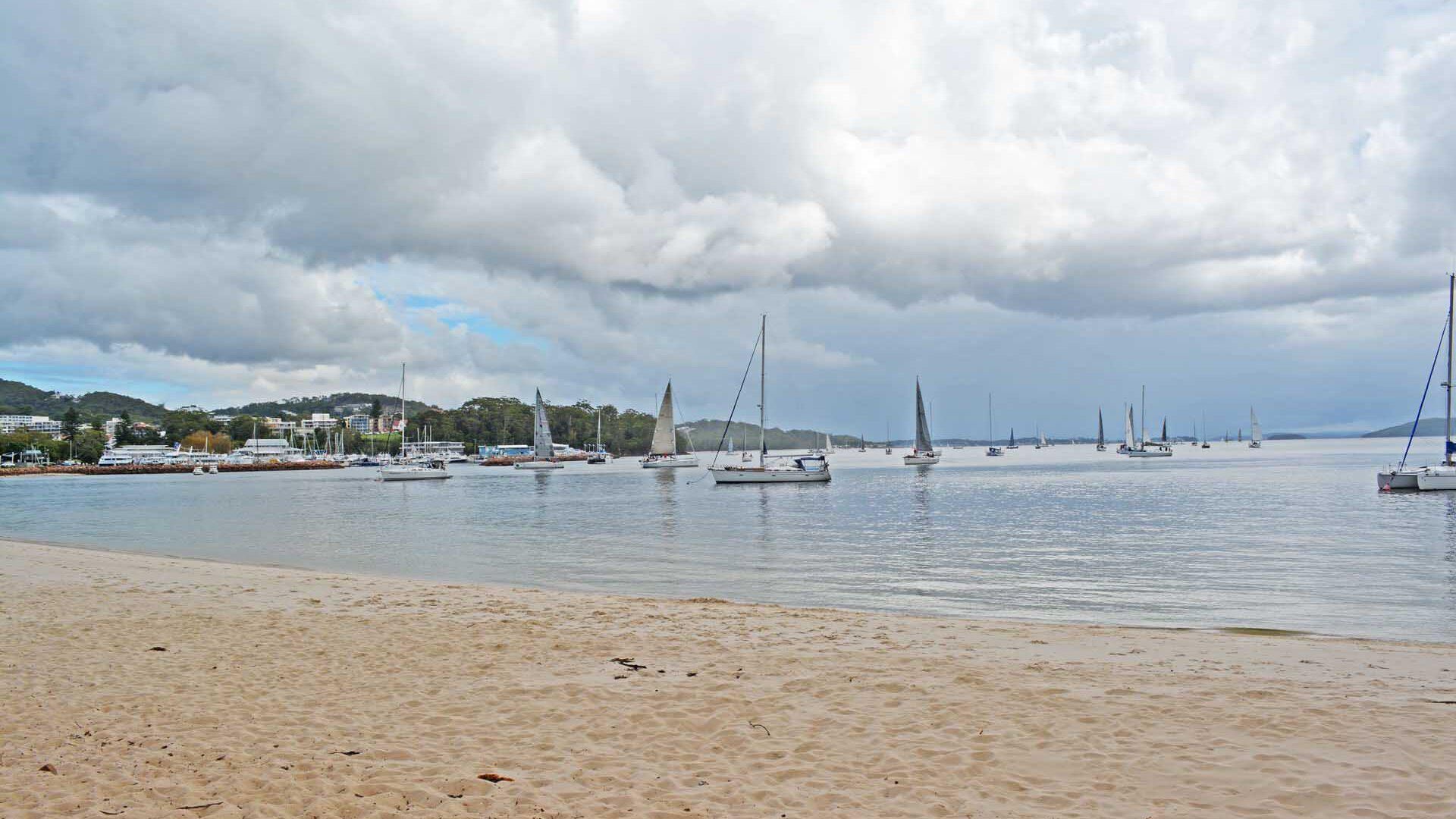 A beach with sailboats and a cityscape in the background.