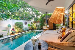 A modern outdoor pool area with a seating area, surrounded by lush greenery and a large woven lamp. - Villa Lora by Villa Finder (Ubud)