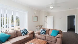 A living room with two brown leather sofas, a wooden coffee table, and a ceiling fan. - Sandy Shoal, 46 Rigney Street - Shoal Bay Beach Cottage with aircon (Shoal Bay)