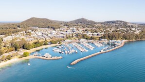 An aerial view of a coastal town with a marina, residential buildings, and hilly terrain in the background.