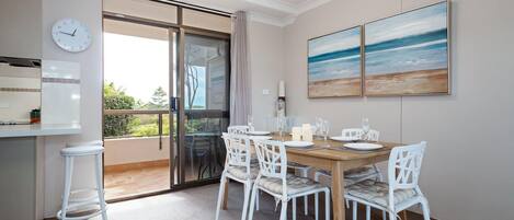 A dining area with a wooden table, white chairs, and a view through a glass door to the outdoors.