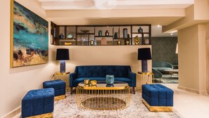 Ein modernes Wohnzimmer mit einem blauen Sofa, passenden Hocker, einem goldenen Couchtisch und einem dekorativen Regal mit verschiedenen Gegenständen.