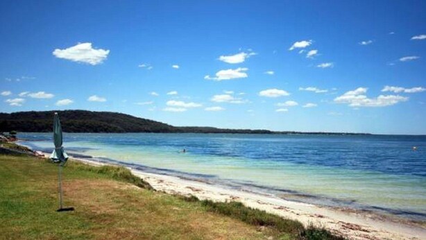 En strand med klart vatten, ett gräsområde och ett avlägset kullområde.