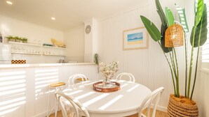 Et spiseområde med et hvidt bord, fire stole, en vase med blomster og en flettet kurv hængende i loftet.