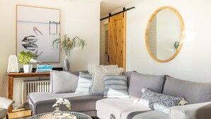 En moderne stue med en grå sofa, en trædør, et rundt spejl og et billede i ramme på væggen.
