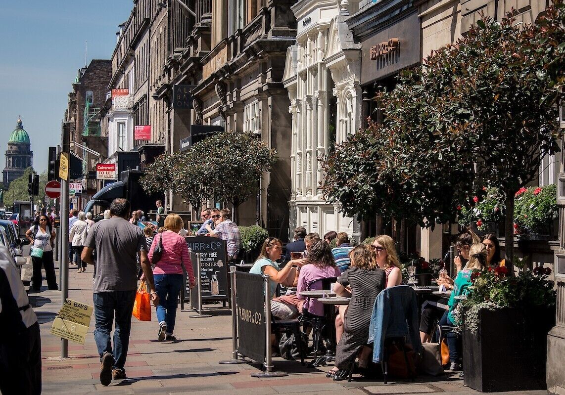 A busy street with outdoor seating at a restaurant, pedestrians, and historic buildings.