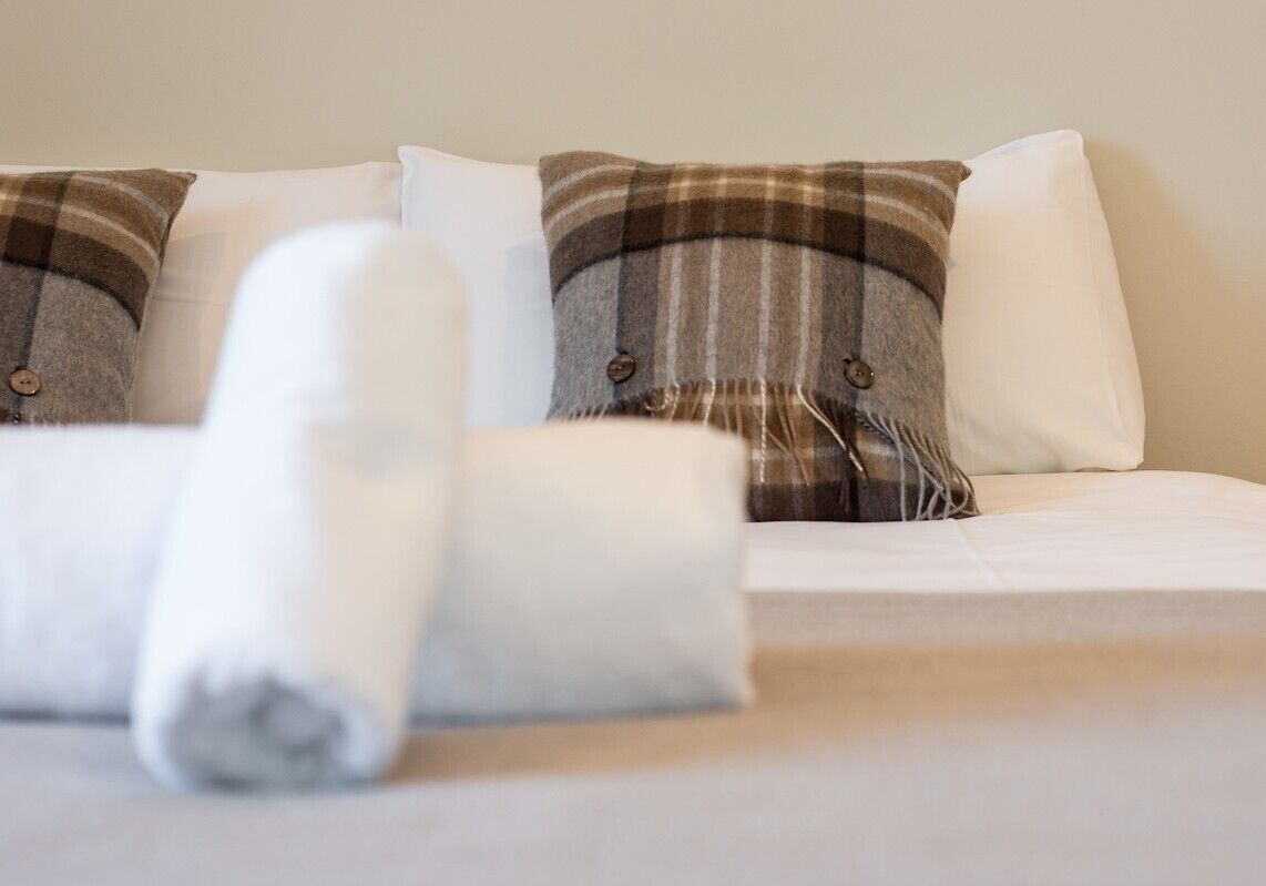 A bed with white bedding and plaid-patterned pillows.