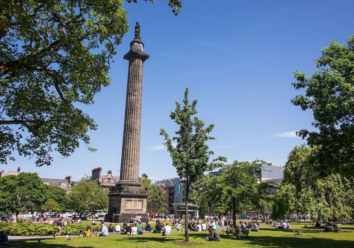A tall monument surrounded by a park with people sitting on the grass.
