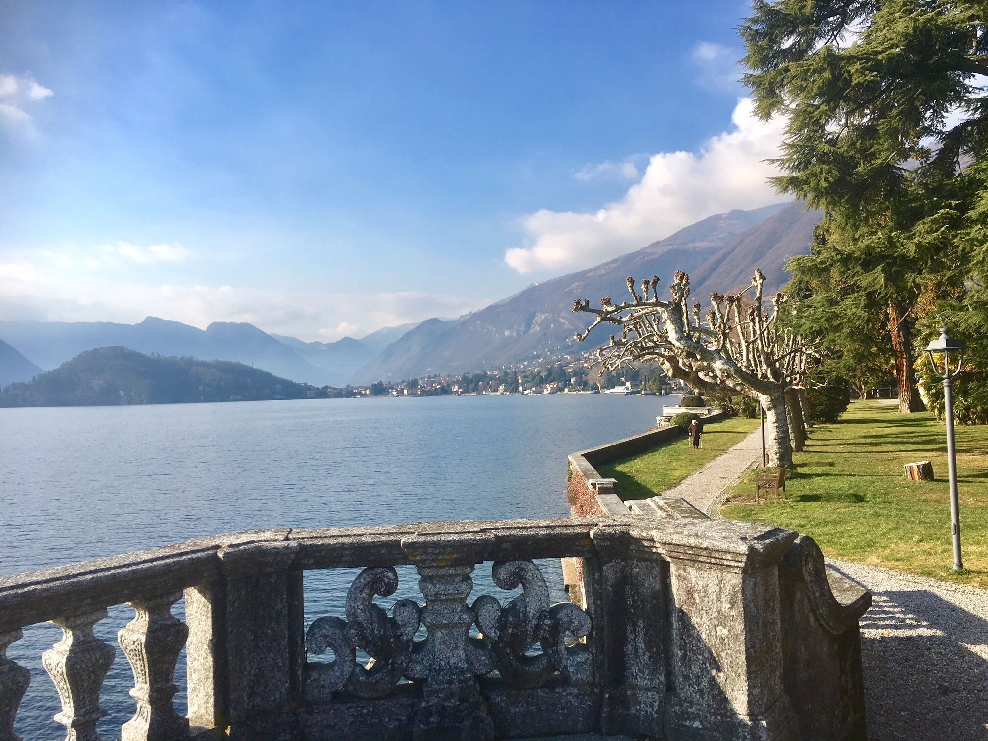 Ein malerischer Seeblick mit Steinbrüstung, einem Pfad und einer baumbestandenen Fläche.