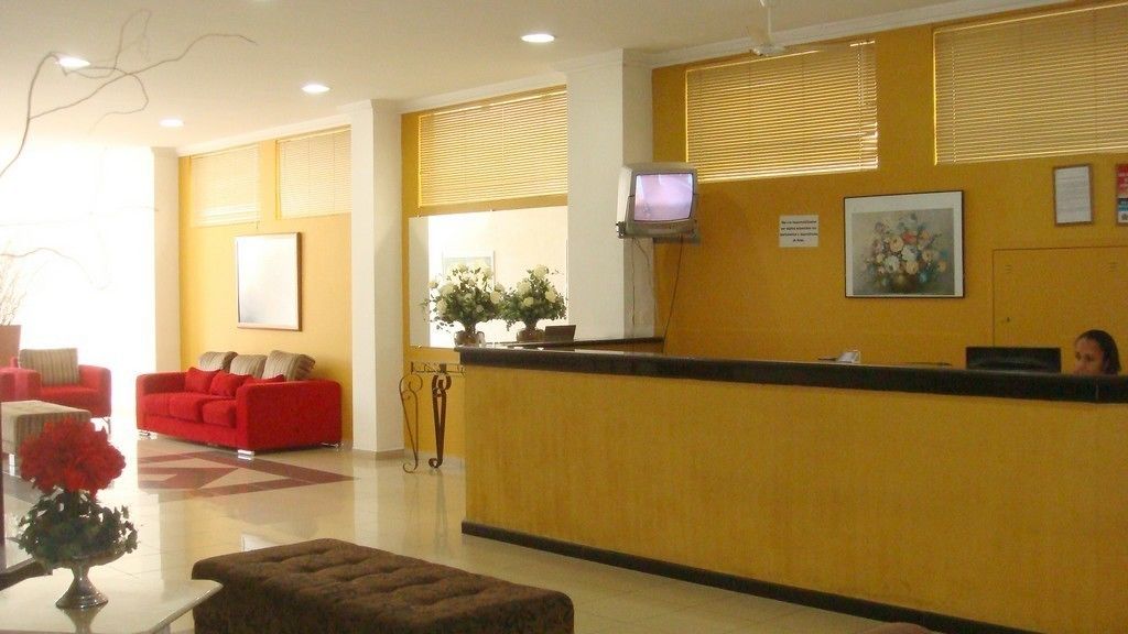 Un área de recepción con pared amarilla, un mostrador de recepción, un sofá rojo y un televisor pequeño en la pared.