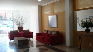 A lobby with two red sofas, a large potted plant, and a framed picture on the wall.