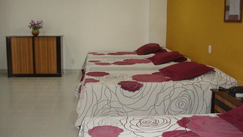 Een hotelkamer met twee bedden, elk voorzien van een bloemenbedekking en rode kussens. Er staat een houten kast met een bloevas erop.