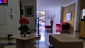 A lobby with a tiled floor, a reception desk, a red sofa, and a television on the wall.